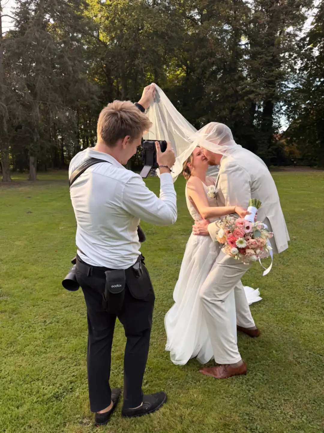 Alex Hartwig fotografiert das Brautpaar, das sich unter dem Schleier küsst