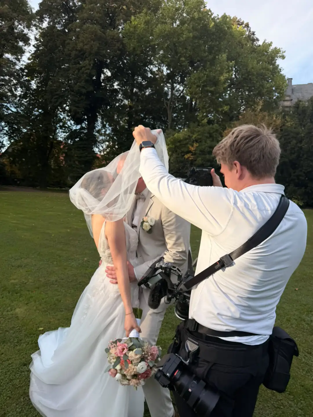 Alex Hartwig hält den Schleier hoch und fotografiert, die Filmkamera hängt am Gurt