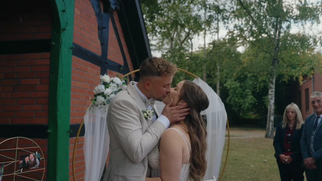 Der Kuss am Traubogen: Standbild aus dem Hochzeitsfilm von Lisa & René